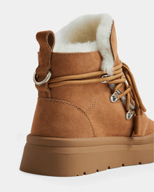 A close-up of the ALEXEY - L225025 Tan women’s winter boot by Rudsak, showing suede material, thick rubber sole, metal eyelets, tan laces, and plush white wool lining around the ankle.