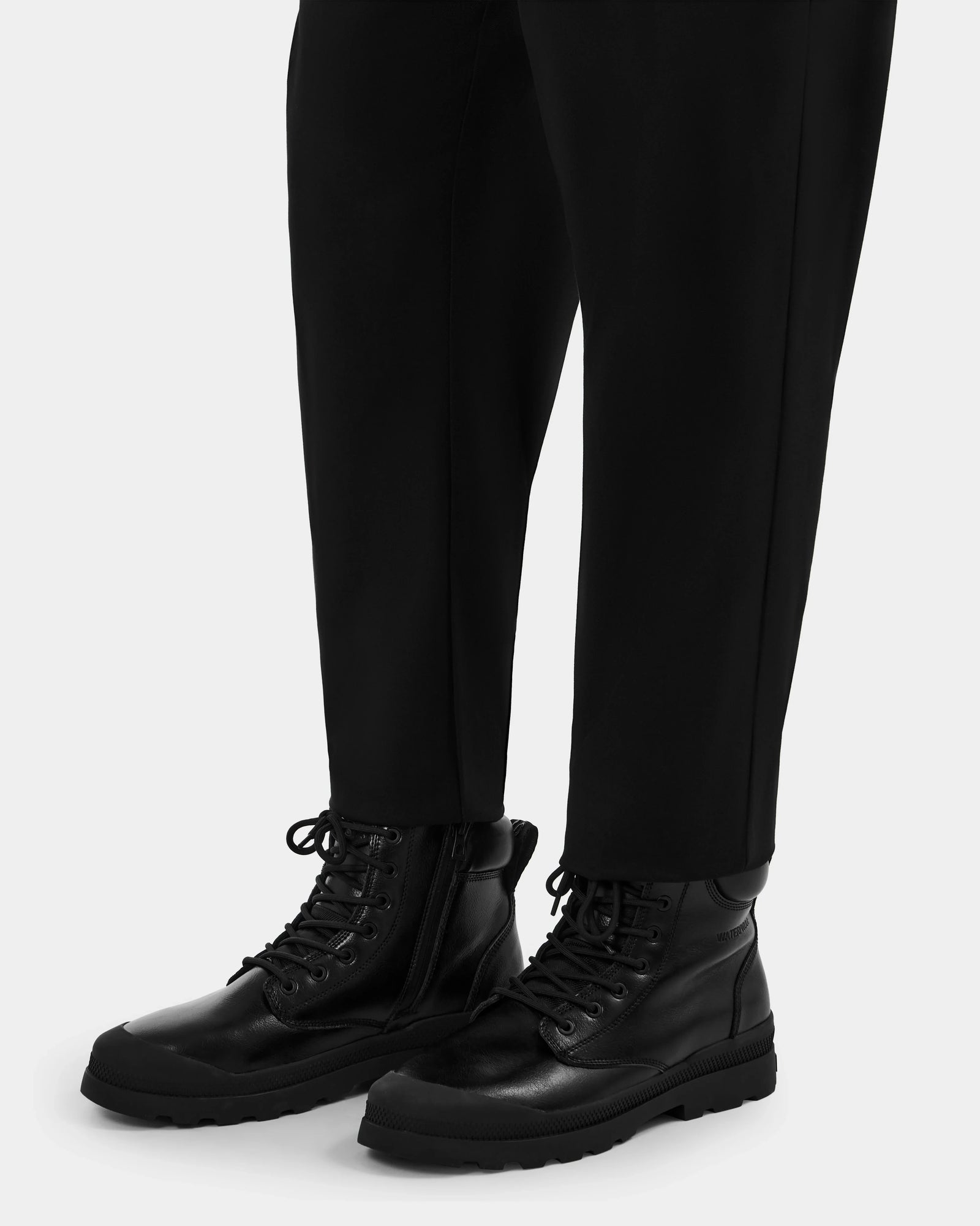 A person wearing Rudsak ARTUR - M223501 Black men's lace-up ankle boots with side zippers and black pants stands against a plain light background.