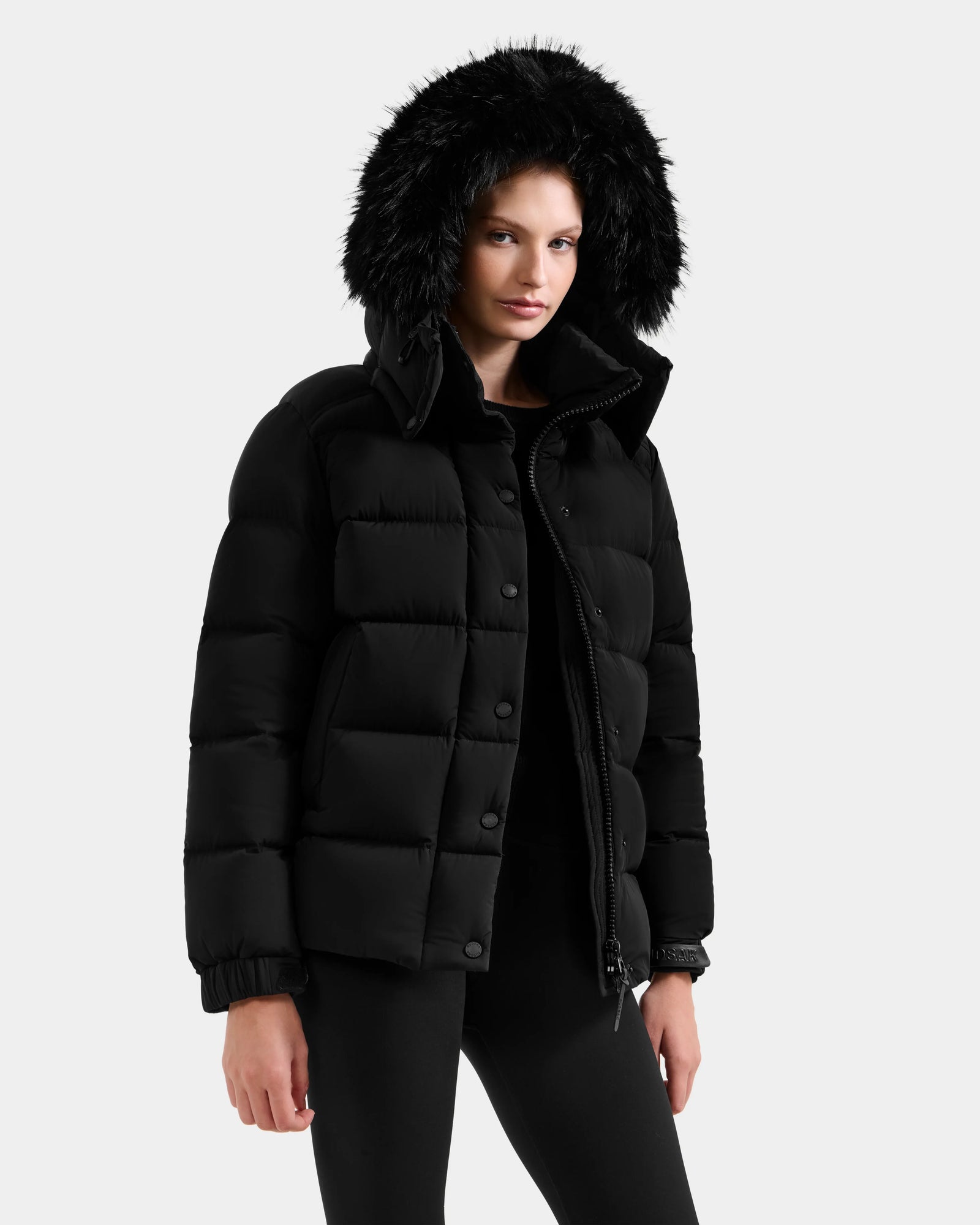 A woman wears the Rudsak BREE M - L125582 Black down puffer coat with a removable hood—an essential cold-weather piece.