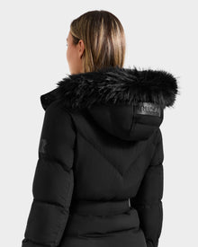 A person with light brown hair is seen from behind wearing the Rudsak CHRISTELLE M - L125542 Black weather-resistant quilted down puffer, featuring a black faux fur-trimmed hood and 