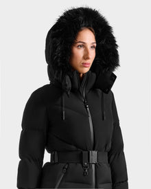 A person models the Rudsak CHRISTELLE M - L125542 Black jacket, a belted, weather-resistant coat with a fur-lined hood, shown against a plain light background.