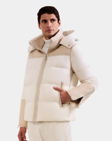 A person wears the Rudsak DAVID - M125508 Vanilla men's off-white shearling puffer jacket with hood and zipper pockets, paired with matching light pants against a plain background.
