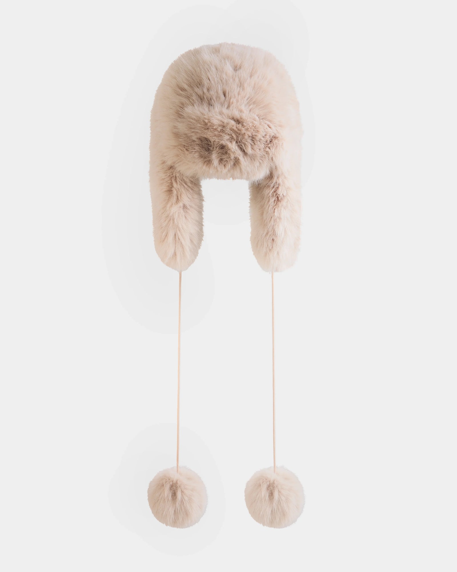 The RUDSAK DEMI - L425539 Vanilla is a beige faux-fur aviator hat with ear flaps and long strings ending in large fur pom-poms, shown against a plain white background.