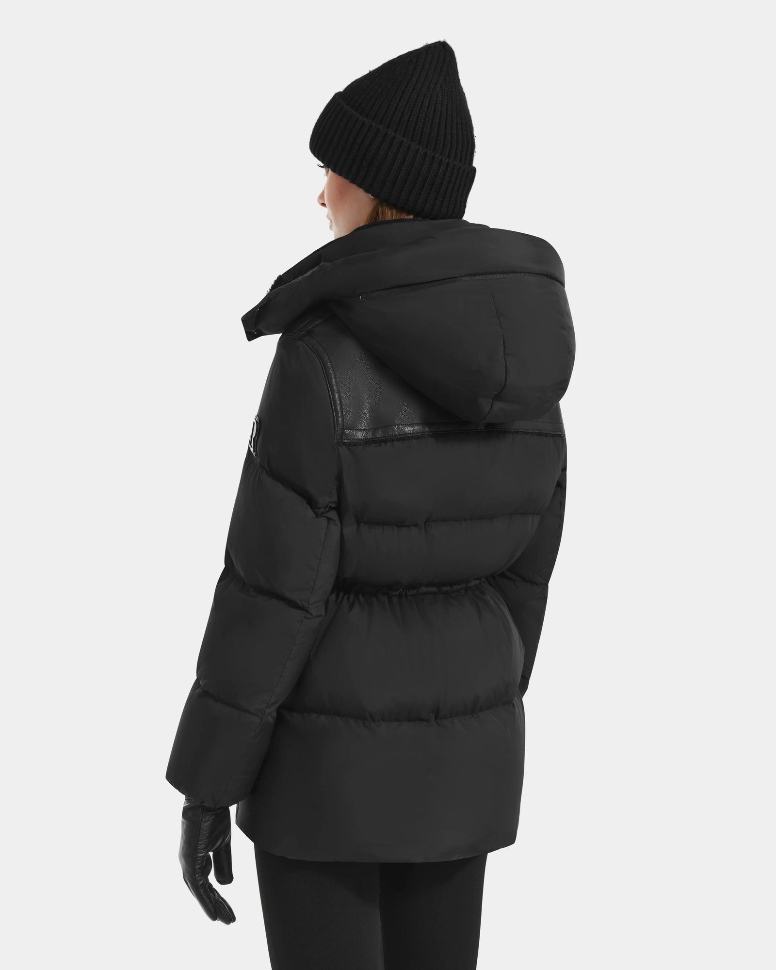 A person is shown from the back wearing Rudsak's EMBER M-M - L125524 Black down puffer with vegan-leather piping, along with a black knit beanie, black gloves, and black pants, all set against a light gray background.