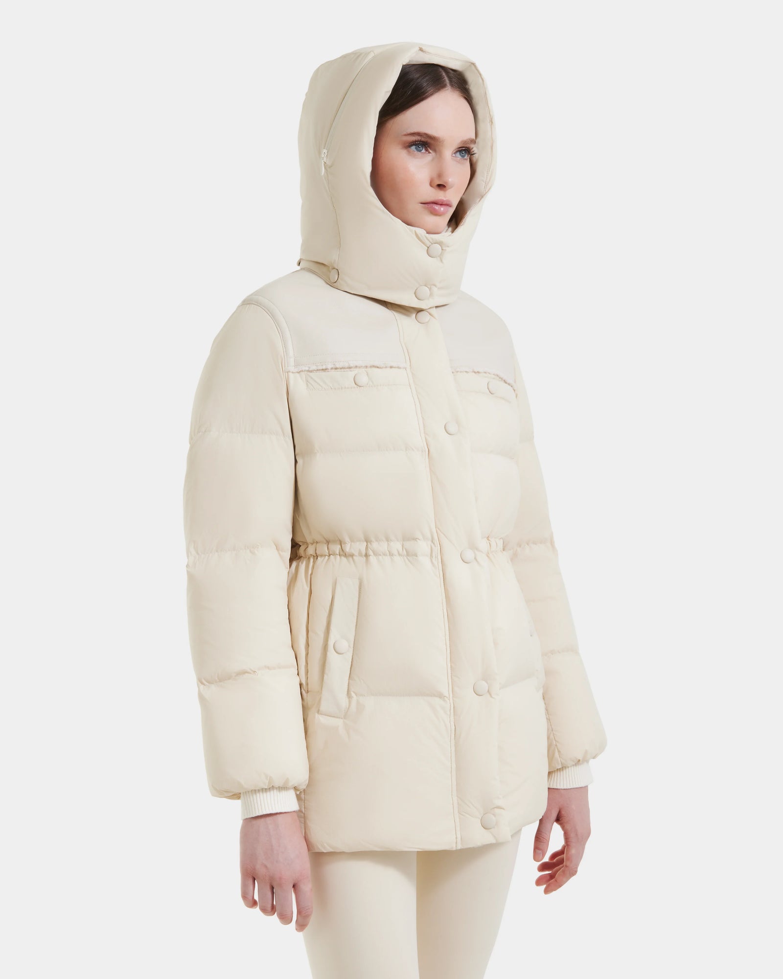 A woman stands against a plain white background wearing the Rudsak EMBER M-M - L125524 Vanilla down puffer jacket with front buttons and pockets.
