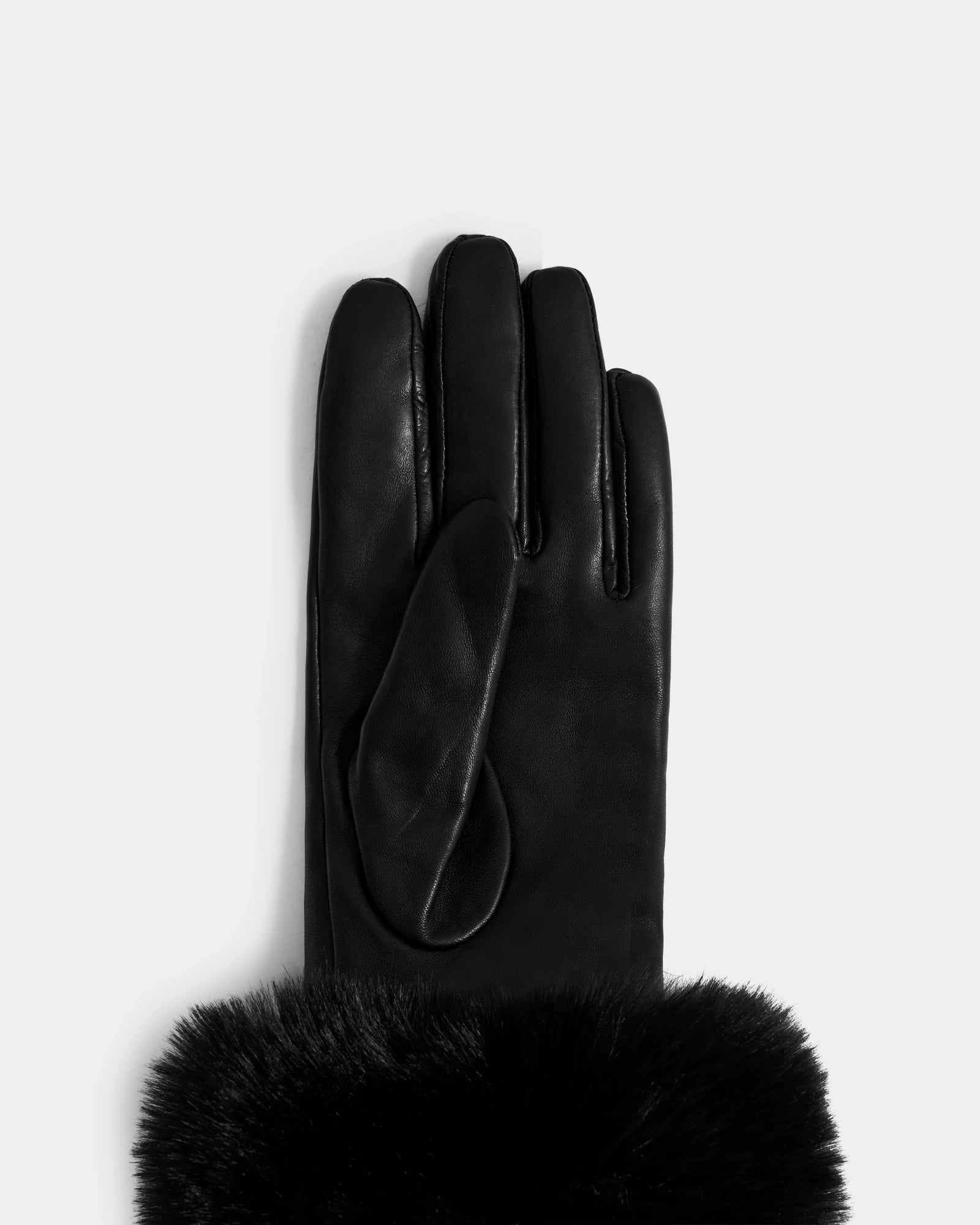 The Rudsak GERRY - L425550 Black women’s glove, crafted from supple lamb leather with a soft black faux-fur cuff, is shown palm down on a light gray background with the fingers and thumb visible.
