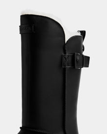 Close-up of the Rudsak KLAIR L - L225519 Black women’s leather boot featuring a white wool-lined interior, side strap with buckle, and brand label near the top—ideal city boots set against a plain gray background.