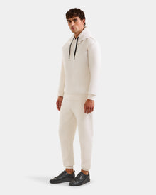 A man with short brown hair wears the Rudsak LEROY - U525509 Vanilla M premium off-white hoodie and matching joggers, paired with black sneakers, standing simply styled against a plain light background.