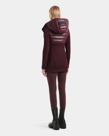 A person in the Rudsak MARRY S - L125521 Wine weather-resistant hooded coat stands facing away, paired with matching maroon leggings and black chunky boots, against a plain white background.