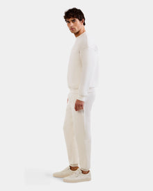 A man stands sideways facing left, wearing the Rudsak MAXTON - U525007 Vanilla M cotton-blend jogger, sweatshirt, and white sneakers against a plain white background for effortless everyday comfort.