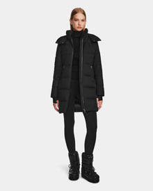 A woman stands facing forward in the Rudsak MIRIAM - L123544 Black womens down puffer coat with RDS-certified down, paired with a black turtleneck, leggings, and winter boots, set against a plain white background.