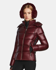 A woman in the Rudsak MIRRY S - L123545 Wine quilted down coat, styled with earmuffs and black leggings, stands against a plain background—a chic and cozy winter look.
