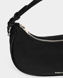 Close-up of the Rudsak NIKKI - L325512 Black women's crescent shoulder bag featuring a gold zipper, adjustable strap, and gold logo on the lower right corner, set against a plain light gray background.