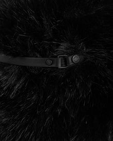 Close-up of Rudsak’s YURI - L425538 Black: black faux fur fabric with vegan-leather trim, a black leather strap, and metal rivets (one engraved), creating a textured, luxurious winter accessory.
