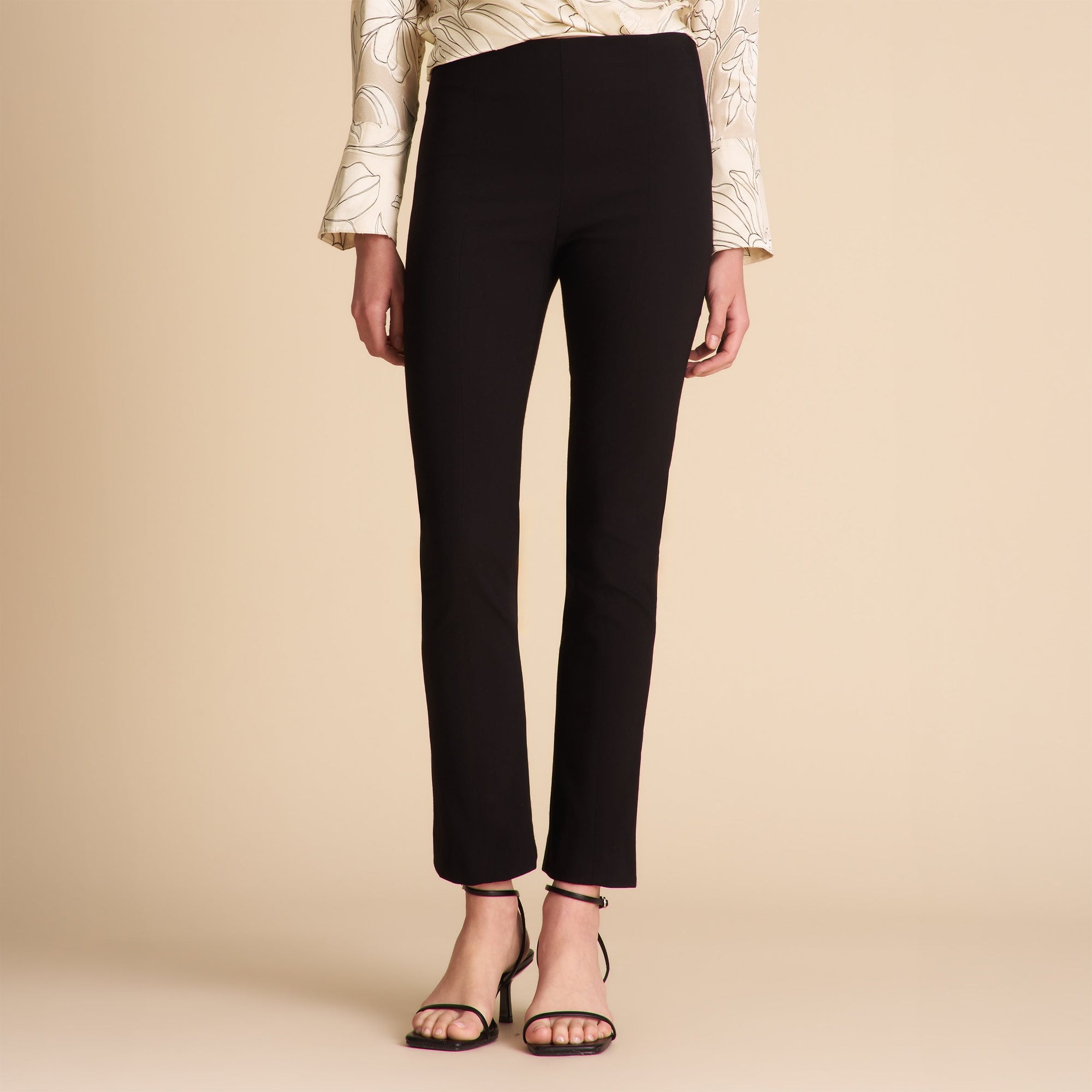 Person wearing black pants and a patterned top on a beige background | Lead