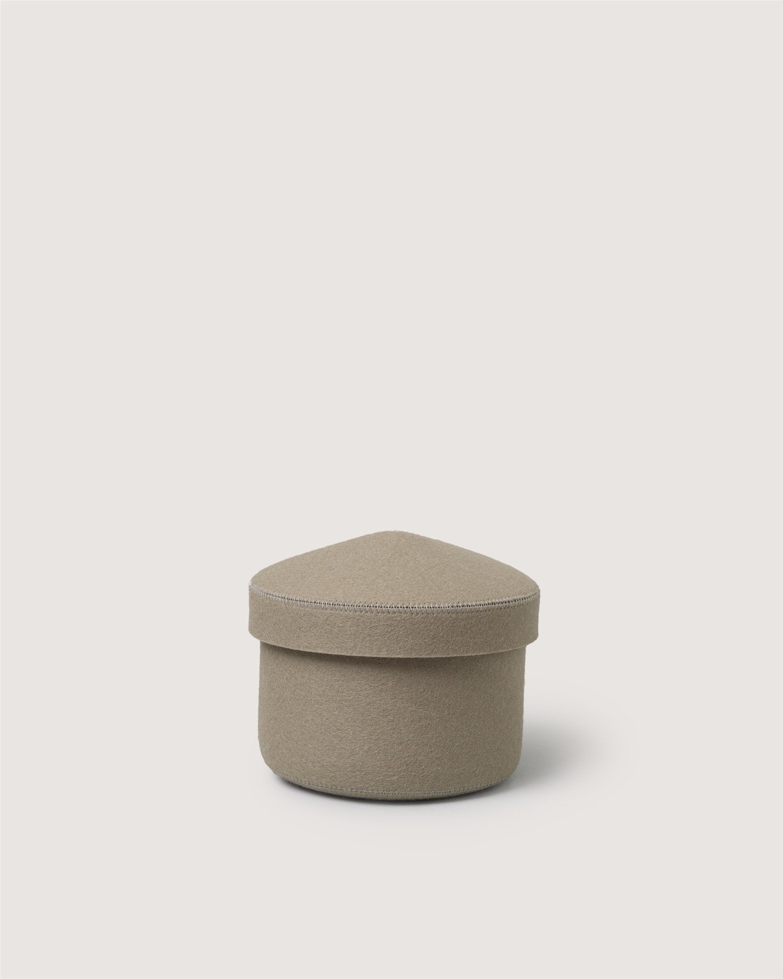 A small, beige Graf Lantz merino wool bin with a fabric cover, round base, and triangular rounded lid sits against a plain light background.