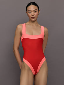 Model wears a high cut one piece square neck bathing suit in red with coral edges. 