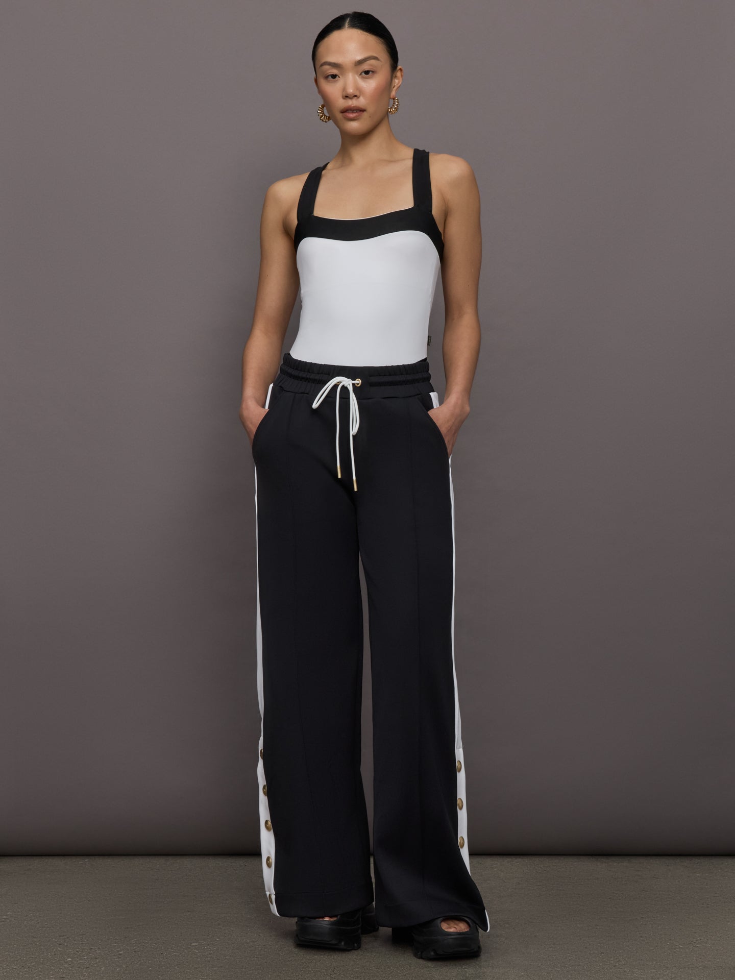 Model wears a high cut one piece square neck bathing suit in white with black edges. 