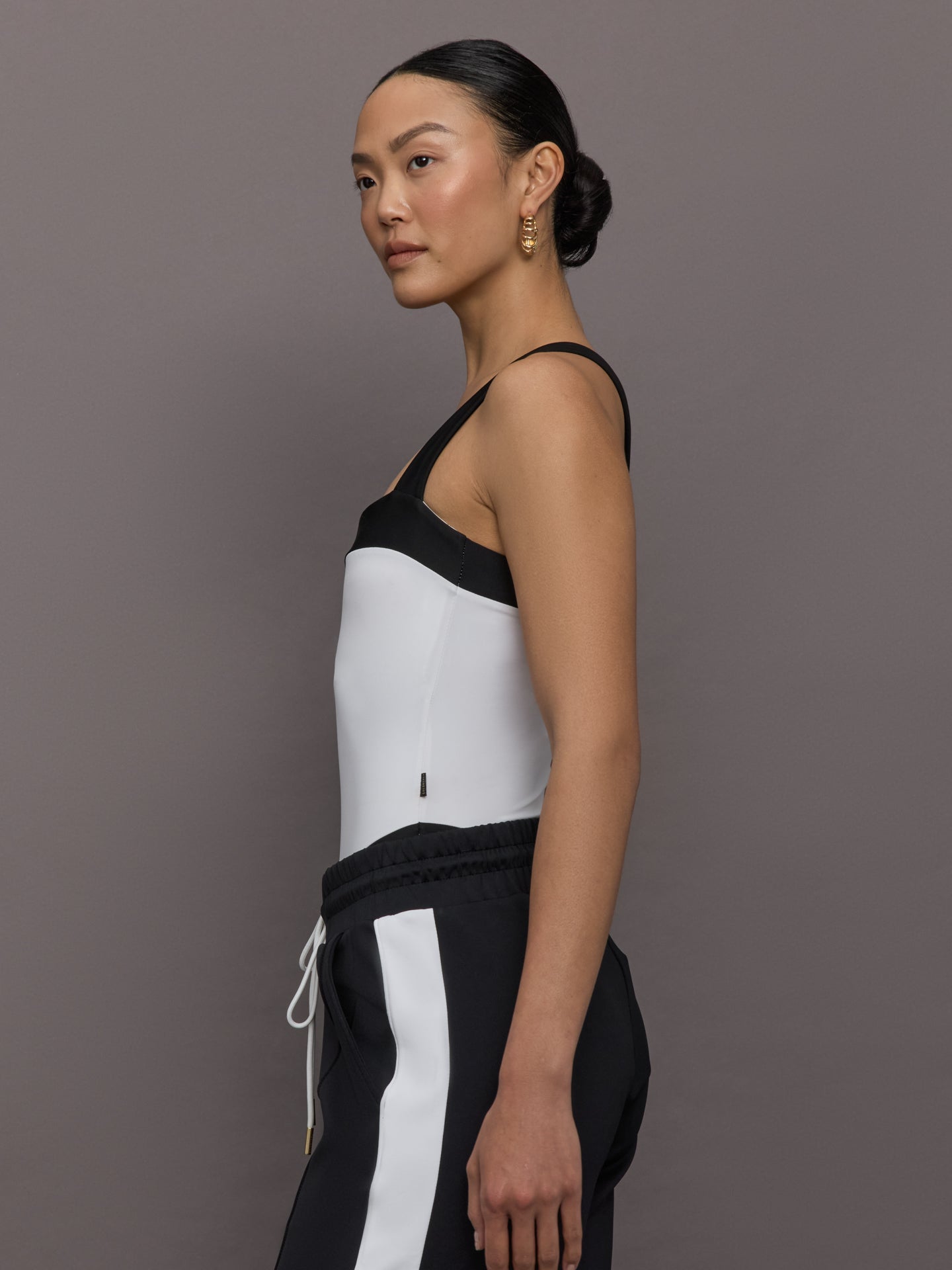 Model wears a high cut one piece square neck bathing suit in white with black edges. 