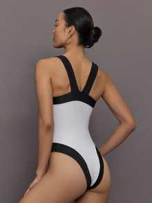 Model wears a high cut one piece square neck bathing suit in white with black edges. 