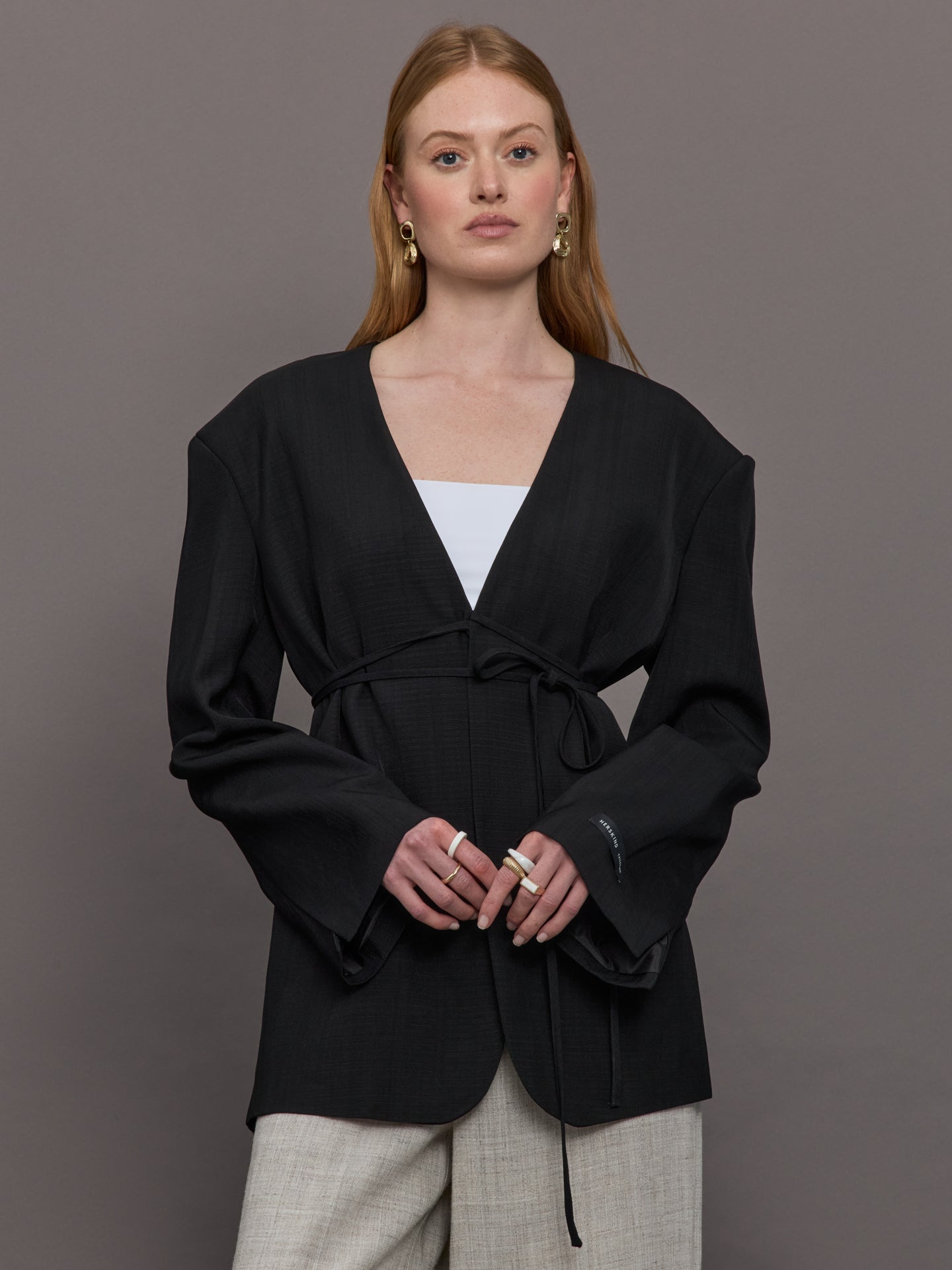 Model wears a wide shoulder black blazer with a deep v neck and drawstring closure. 