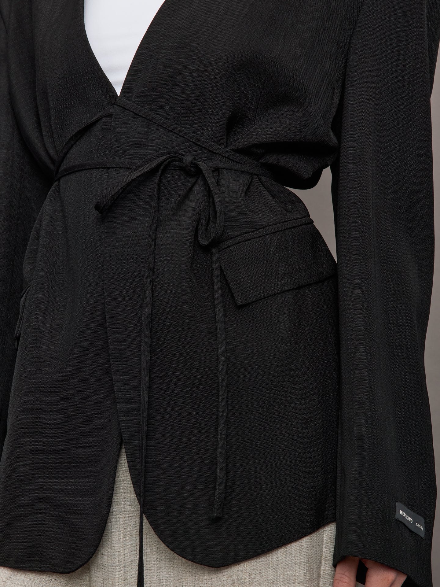 Model wears a wide shoulder black blazer with a deep v neck and drawstring closure. 