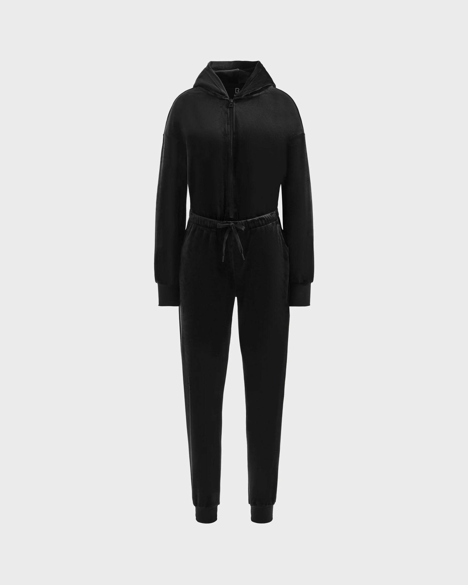 The Rudsak KETZY - L525503 Black women’s velour hooded jumper in black stretch velour features long sleeves, a front zipper, drawstring waist, and cuffed ankles, shown on a plain light gray background.