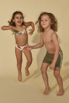 Child wearing khaki and white patterned swim shorts with white stripe detail on the side.