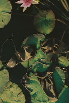 Khaki scrunch bikini bottom with ruched sides displayed on lily pads and pink flower.