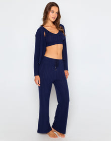 Woman wearing a navy blue ribbed long sleeve cardigan with front buttons, styled open over a matching bralette and pants.