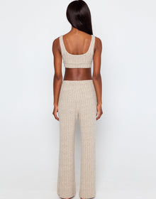 Woman wearing a beige ribbed knit loungewear set, featuring a cropped tank top with a scoop neckline and wide-leg drawstring pants with side pockets, standing barefoot against a plain white background.