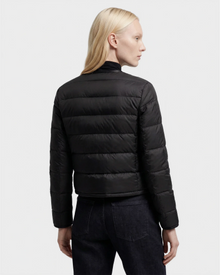 A person with long blond hair, seen from the back, wears the MARKLE - 8125033 Black women’s cropped down jacket by Rudsak with vegan leather trim and dark jeans against a plain light background.