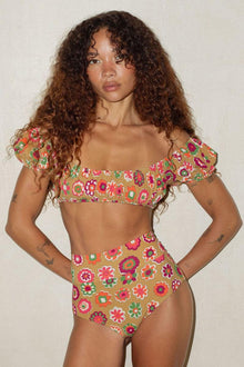 Floral print bikini top with ruffled off-shoulder neckline in multicolored flowers on tan background.