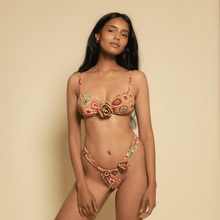Woman wearing multicolored floral bikini with gold rose-shaped hardware details on chest and hip areas.