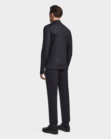 A man faces away from the camera, wearing the Rudsak WARREN - 6523502 Black Pattern fleece-lined zip-front mock neck jacket, black pants, and black shoes against a plain light gray background.