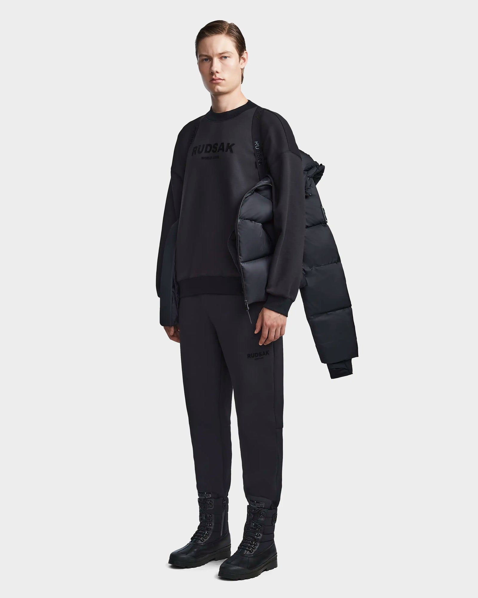 A man wearing the Rudsak DANIEL M - M123510 BLACK weather-resistant winter jacket and black pants.