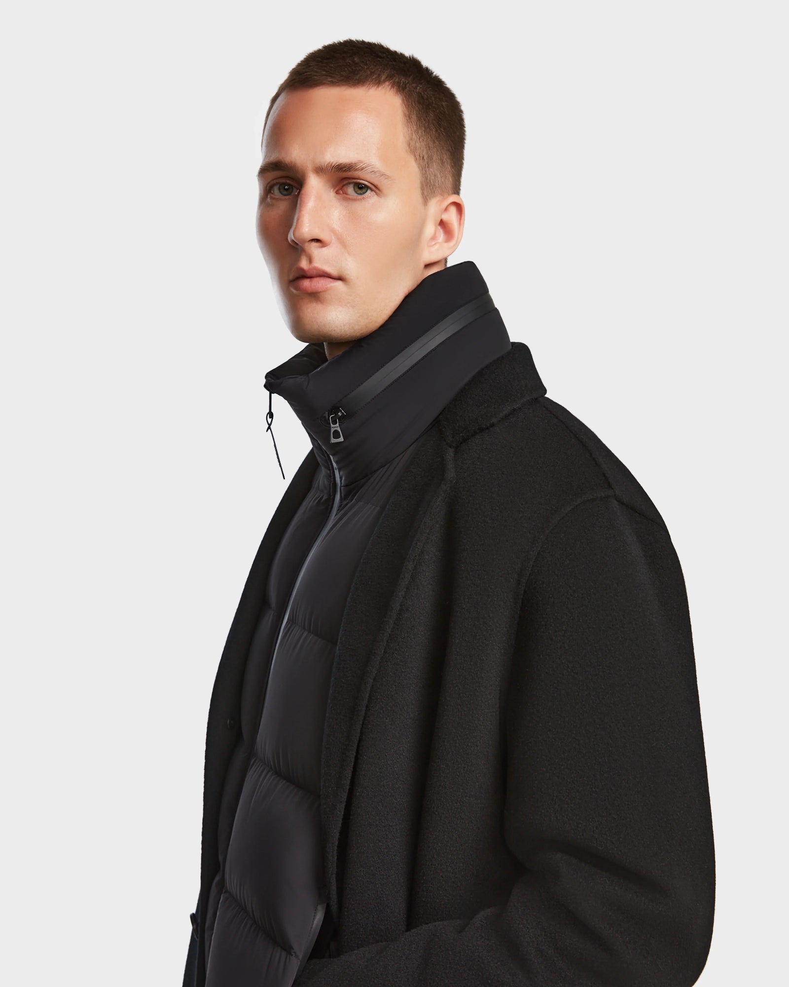 A man with short hair wears the Rudsak DRAL - 6124503 Black down puffer under a dark mens wool jacket, looking slightly to the side against a plain white background.