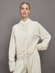 Model wears an oversized cream colored hoodie with extra long drawstrings. 