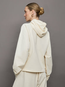 Model wears an oversized cream colored hoodie with extra long drawstrings. 
