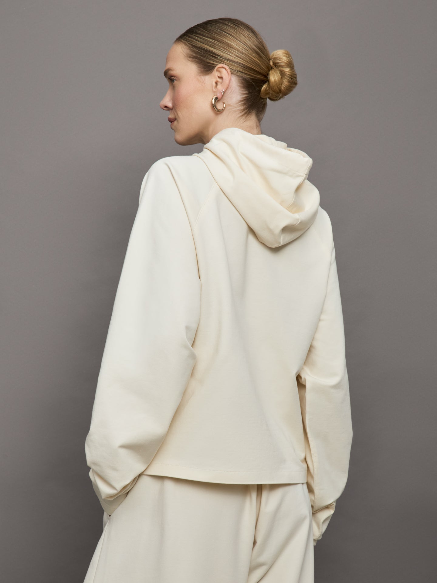 Model wears an oversized cream colored hoodie with extra long drawstrings. 