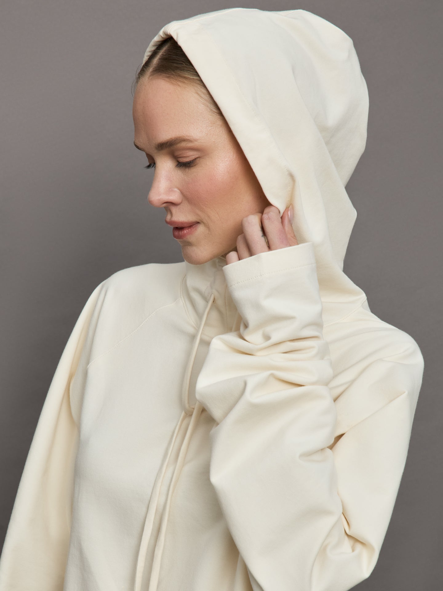 Model wears an oversized cream colored hoodie with extra long drawstrings. 