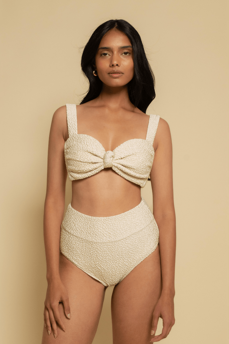 Cream textured bikini top with sweetheart neckline, bow detail at center, and thick shoulder straps.