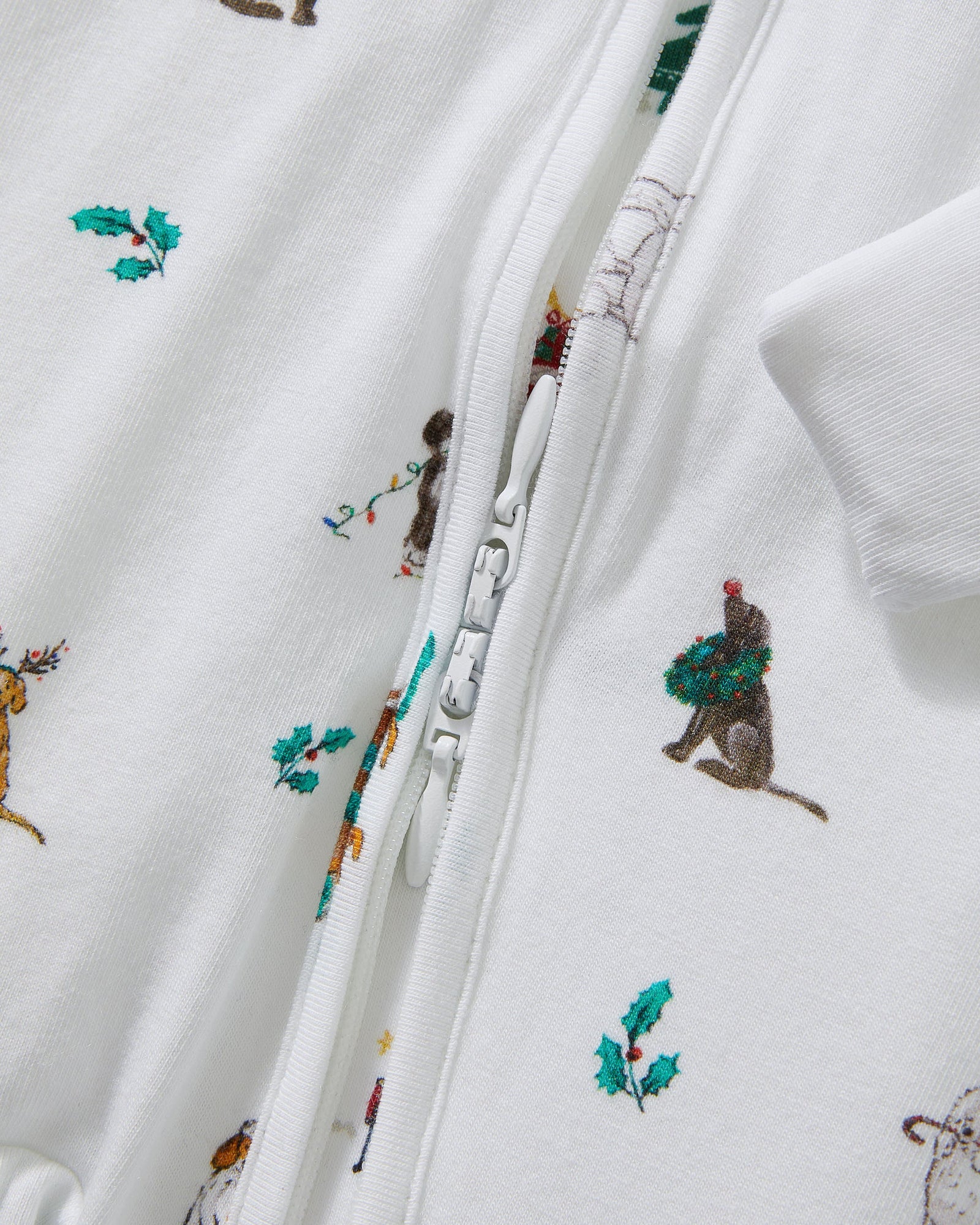 The Baby's Pima Peekaboo Romper in Jingle Paws is a white, long-sleeve onesie with a front zipper, decorated with colorful dogs and green bones. The left leg appears slightly folded over.