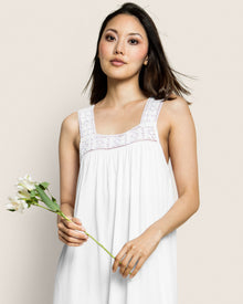 A woman in a white, sleeveless dress with lace details holds a bouquet of white flowers, akin to the elegance of Petite Plumes Womens Pima Camille Nightgown in White. She has shoulder-length hair and gazes calmly at the camera against a plain background.