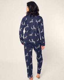 A person with dark hair stands barefoot, facing away, wrapped in a Womens Pima Pajama Set in Zebre de Nuit by Petite Plume, featuring luxury navy-blue zebra print on an off-white background.