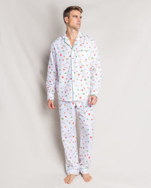 A person stands against a plain background wearing Petite Plumes Mens Twill Pajama Set in Shades of Autumn, featuring a collar, buttons, and a pocket with green piping. Barefoot, the person gazes thoughtfully to the side.