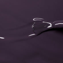 A close-up of the Manucurist Queen of Night brush applying glossy dark violet gel polish with gray undertones, reflecting light and enhancing depth on a smooth surface.