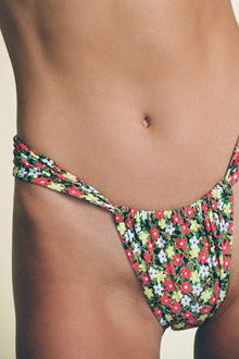Bikini bottom with red, yellow, and white floral print on dark background, gathered sides.