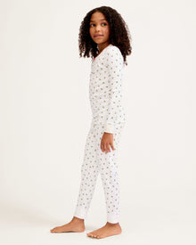 Kid's Pima Snug Fit Pajama Set in Mistletoe Moments: a two-piece white pajama set for children with a long-sleeve top, pants, green and red holly pattern, red scalloped neckline, and a red bow at the collar.