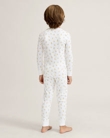 A young child with light brown hair stands barefoot on a plain background, wearing the Kid's Pima Snug Fit Pajama Set in Tres Chick and looking slightly to the side.